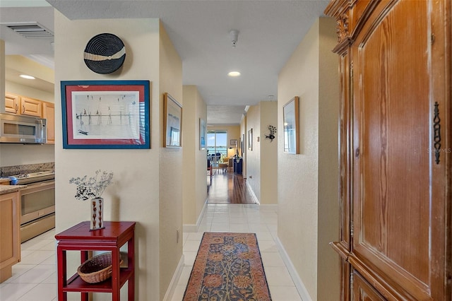 hallway with light tile patterned flooring, visible vents, and baseboards