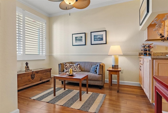 sitting room featuring light wood-type flooring, baseboards, a ceiling fan, and crown molding