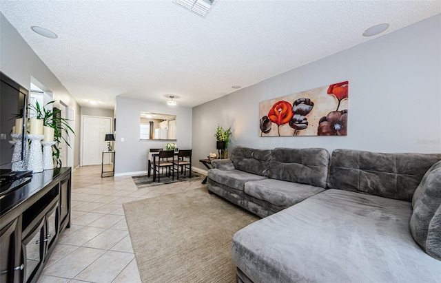 living room with light tile patterned flooring, visible vents, a textured ceiling, and baseboards