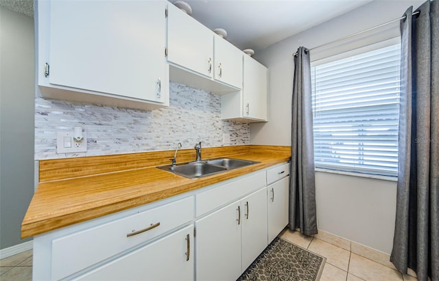 kitchen featuring light tile patterned flooring, a sink, decorative backsplash, light countertops, and white cabinetry