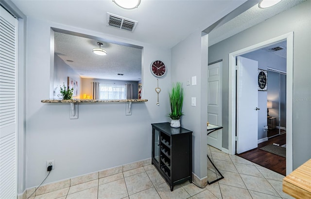 hall with light tile patterned flooring, visible vents, and a textured ceiling