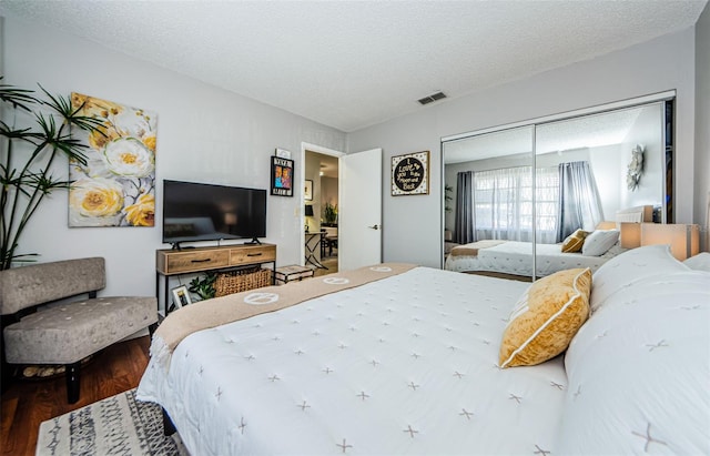 bedroom featuring a closet, visible vents, a textured ceiling, and wood finished floors