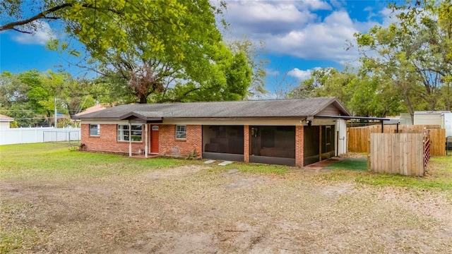 view of front of property featuring fence, brick siding, a front lawn, and a sunroom