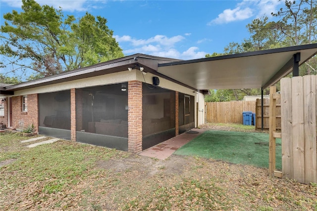 view of side of property featuring brick siding, fence, a lawn, and a sunroom