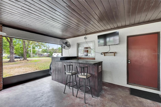 exterior space with wood ceiling, concrete floors, a dry bar, and a textured wall