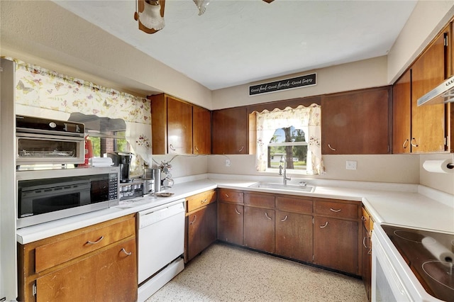 kitchen with a sink, white appliances, brown cabinets, and light countertops