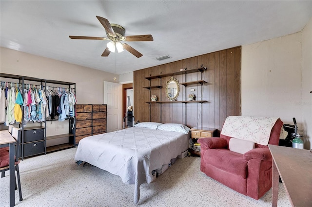 bedroom with ceiling fan, visible vents, wood walls, and speckled floor