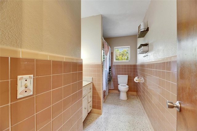 full bathroom with a shower with curtain, a wainscoted wall, speckled floor, tile walls, and toilet