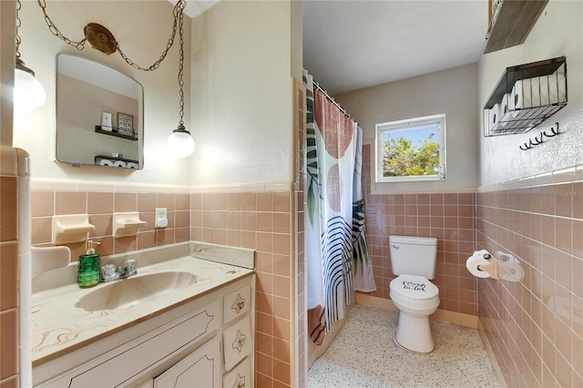 bathroom with toilet, tile walls, wainscoting, speckled floor, and vanity