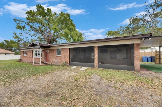 rear view of house with a yard, a sunroom, brick siding, and fence