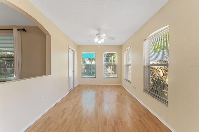 empty room with plenty of natural light, baseboards, light wood-type flooring, and ceiling fan