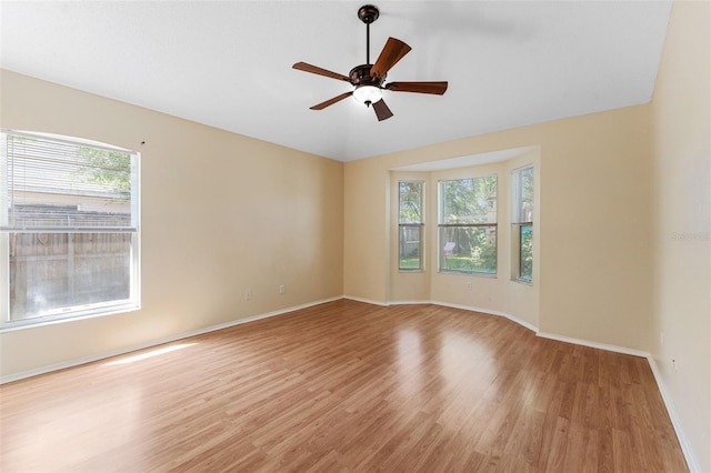 spare room featuring light wood finished floors, a healthy amount of sunlight, baseboards, and ceiling fan