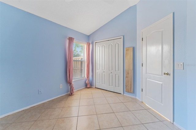 unfurnished bedroom featuring lofted ceiling, light tile patterned flooring, baseboards, and a closet