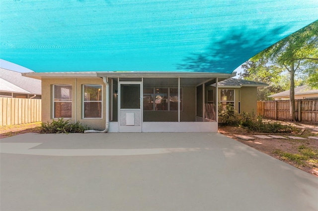 back of property featuring stucco siding, concrete driveway, fence, and a sunroom