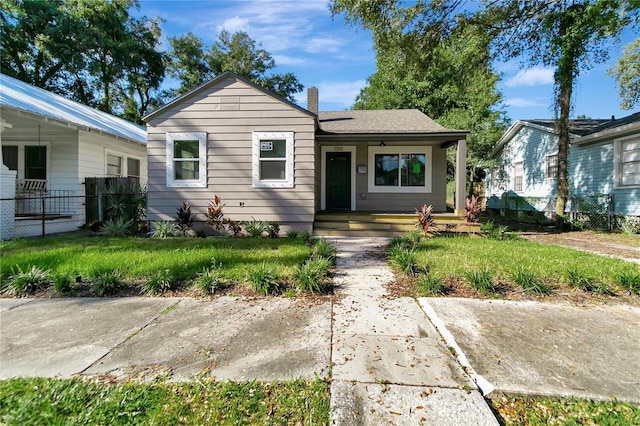 view of front facade featuring a front yard, fence, covered porch, and a chimney