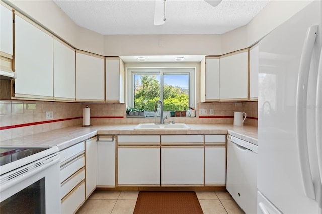 kitchen with white appliances, white cabinets, light tile patterned flooring, and a sink