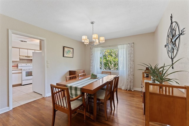 dining space featuring light wood finished floors, a chandelier, a textured ceiling, and baseboards