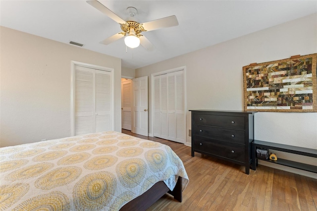 bedroom with a ceiling fan, wood finished floors, visible vents, and multiple closets