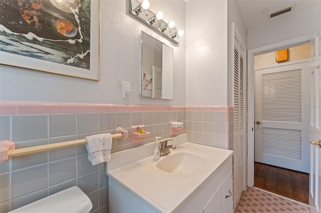 half bath with visible vents, tile walls, a wainscoted wall, toilet, and vanity