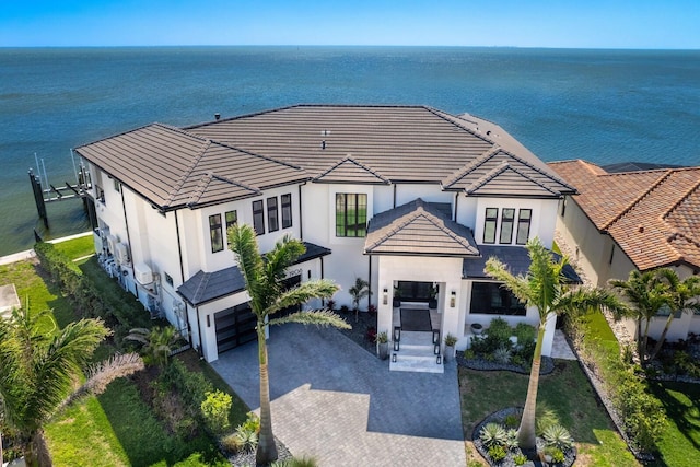 view of front facade featuring stucco siding, a tile roof, decorative driveway, and a water view