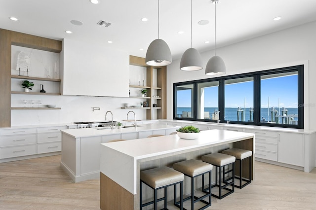 kitchen featuring visible vents, a center island with sink, open shelves, light wood finished floors, and light countertops