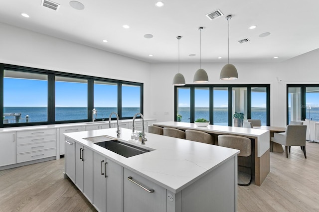 kitchen featuring visible vents, a center island with sink, light wood-type flooring, and a sink