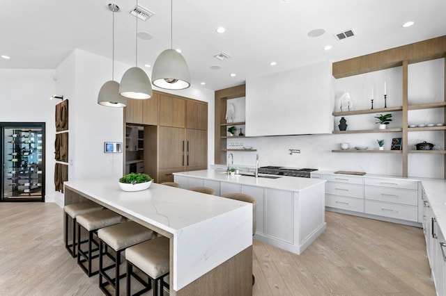 kitchen featuring visible vents, light wood-type flooring, modern cabinets, an island with sink, and open shelves