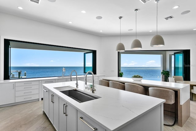 kitchen with a center island with sink, light wood-style floors, visible vents, and a sink