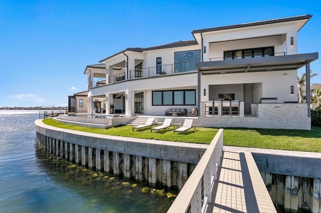 rear view of house with a balcony, a yard, stucco siding, a water view, and a patio area