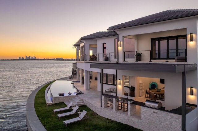 back of house with a tile roof, exterior kitchen, stucco siding, a balcony, and a patio area