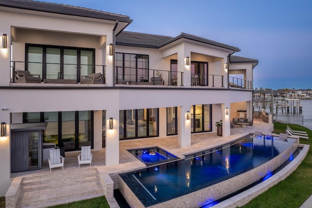 back of house with a patio area, stucco siding, a pool with connected hot tub, and a balcony