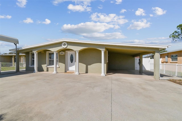 view of front of home with stucco siding, a carport, concrete driveway, and fence