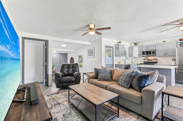 living room with a textured ceiling, ceiling fan, and light wood finished floors