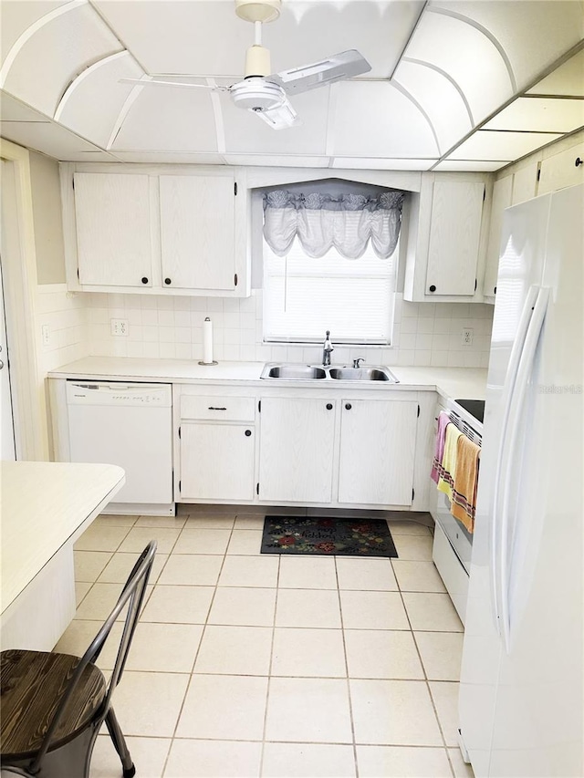 kitchen featuring a sink, tasteful backsplash, white appliances, light countertops, and light tile patterned floors