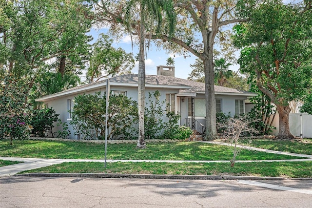 ranch-style house featuring stucco siding, a chimney, a front lawn, and fence