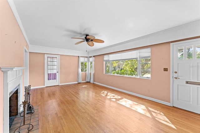 unfurnished living room featuring light wood finished floors, a fireplace with raised hearth, baseboards, ornamental molding, and a ceiling fan