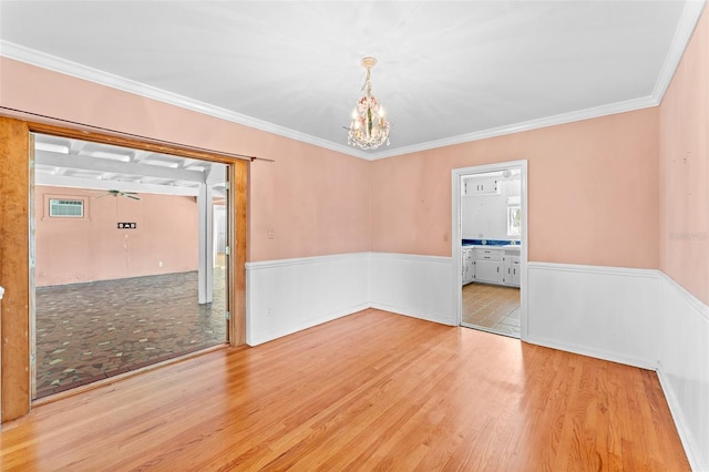 unfurnished room with crown molding, a notable chandelier, wood finished floors, and a wainscoted wall