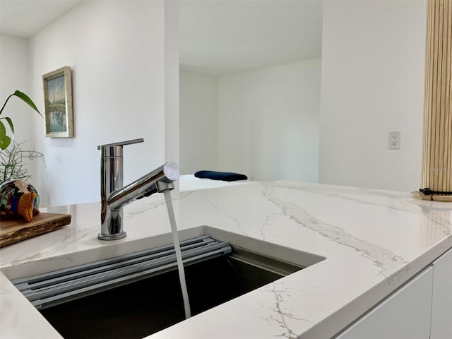 room details with white cabinetry, light stone counters, and a sink