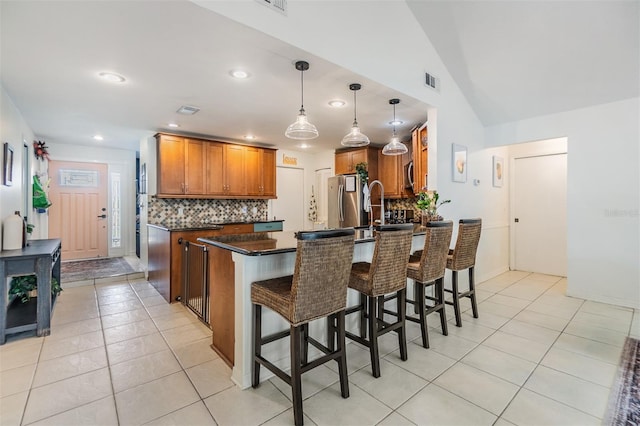 kitchen featuring tasteful backsplash, visible vents, a peninsula, freestanding refrigerator, and brown cabinetry