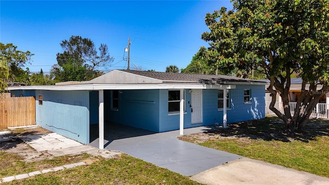 view of front of property featuring a carport, concrete block siding, driveway, and fence