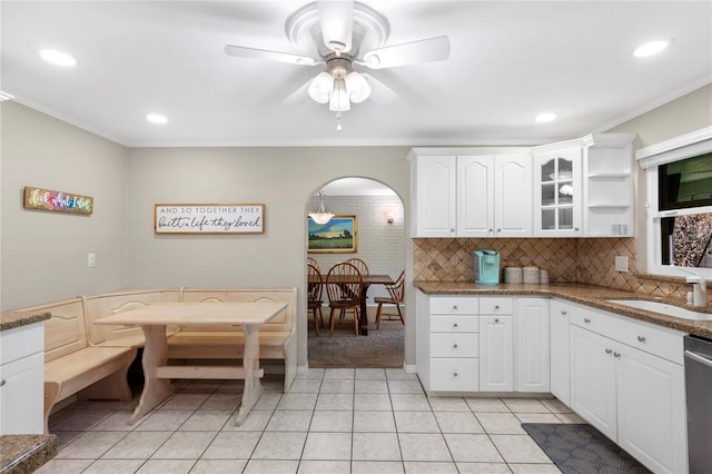 kitchen featuring arched walkways, ornamental molding, backsplash, and a sink