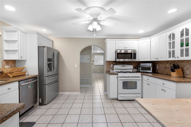 kitchen with light tile patterned floors, stainless steel appliances, arched walkways, white cabinetry, and open shelves