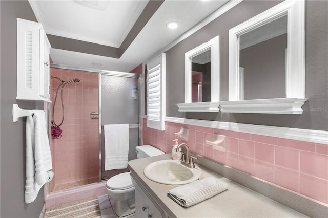 bathroom featuring a shower stall, crown molding, toilet, vanity, and tile walls