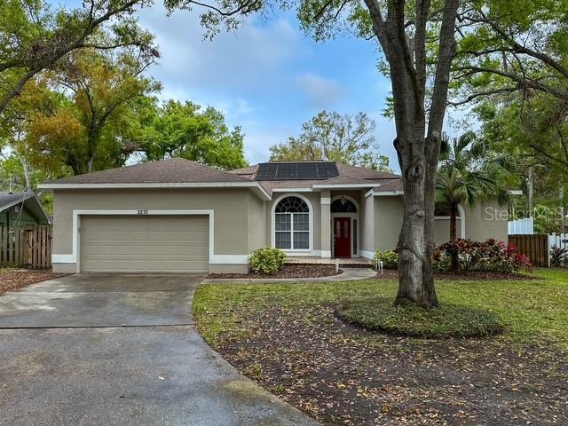 ranch-style home featuring roof mounted solar panels, stucco siding, a garage, and fence