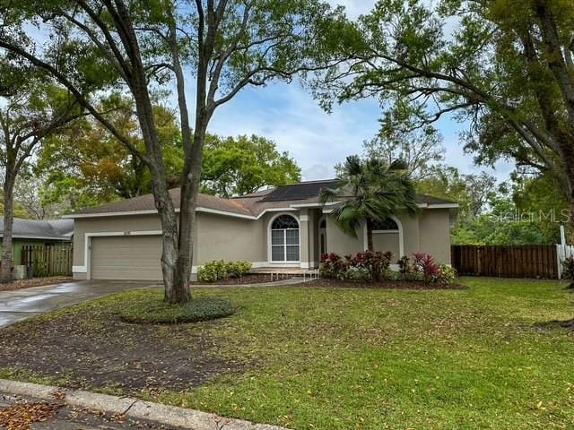 ranch-style house with a front yard, fence, driveway, an attached garage, and stucco siding