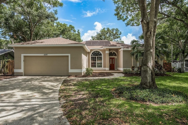 mediterranean / spanish-style house with driveway, an attached garage, stucco siding, a front lawn, and roof mounted solar panels