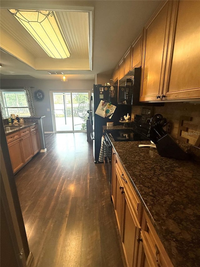 kitchen featuring a tray ceiling, black appliances, dark wood finished floors, and brown cabinetry