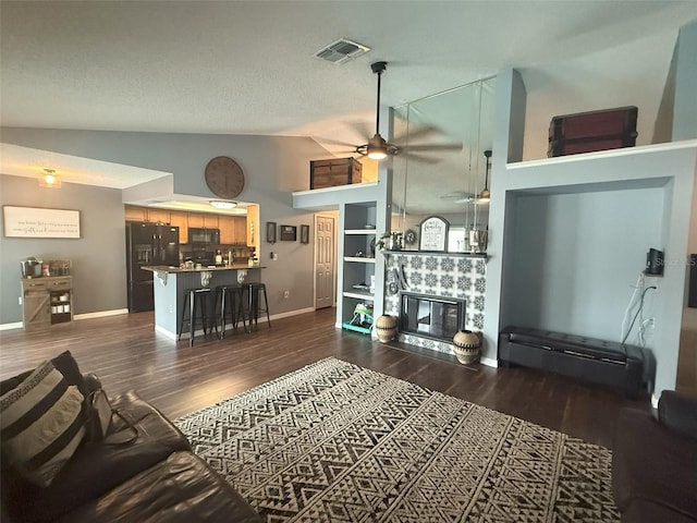 living room featuring a tiled fireplace, dark wood-style floors, a ceiling fan, and visible vents