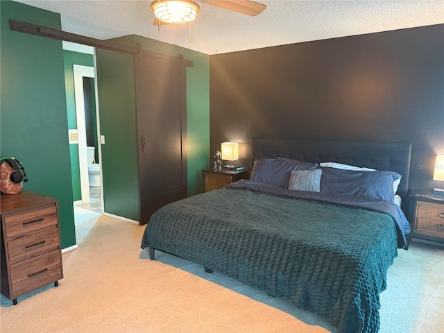 bedroom featuring a ceiling fan, ensuite bathroom, a textured ceiling, a barn door, and light colored carpet