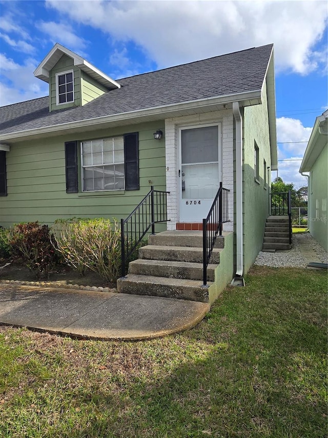 view of front of house featuring entry steps, a front lawn, brick siding, and a shingled roof